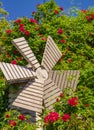 A small wooden windmill in the beautiful summer garden. Windmill and roses. Garden furniture Royalty Free Stock Photo