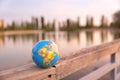 Small world globe placed on the wooden fence of a large lake