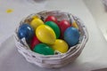 A small woven basket full of brightly colored Easter eggs in blue, yellow, green and red. The basket is placed on a light, Royalty Free Stock Photo