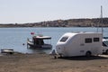 Small yacht while caravan and car in the back on the beach. At the back is the sea and summer houses