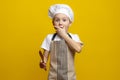 small 6-7 year old boy holding a wooden spoon with an expression of surprise on a pastel yellow background. kid cook Royalty Free Stock Photo