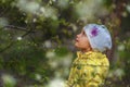 Small 5 years old girl looking up for blooming tree. Child in yellow coat and white hat looks on flowers in blossom garden in Royalty Free Stock Photo