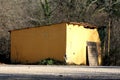 Small yellow abandoned storage area with dilapidated facade partially covered with crawling plants and broken entrance doors