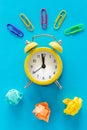 Small yellow alarm clock on blue background, Colorful office staples and crumpled paper balls. Top View. The concept of office wor Royalty Free Stock Photo