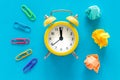 Small yellow alarm clock on blue background, Colorful office staples and crumpled paper balls. Top View. The concept of office wor Royalty Free Stock Photo