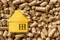 Small yellow house against wooden pellets background macro. Compacted sawdus as organic biofuel. Alternative ecological heating, Royalty Free Stock Photo