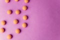 Small yellow orange beautiful medical pharmaceptic round pills, vitamins, drugs, antibiotics on a pink purple background, texture. Royalty Free Stock Photo