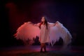 Small young model girl with white wings posing and dancing in dark black studo during photoshoot with flour or dust and colour Royalty Free Stock Photo