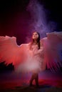 Small young model girl with white wings posing and dancing in dark black studo during photoshoot with flour or dust and colour Royalty Free Stock Photo