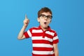 Smart amazed little boy in eyeglasses opening mouth and pointing up while having idea against blue Royalty Free Stock Photo