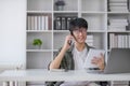 Smart Asian businessman in casual clothing using smartphone and laptop computer working at home office. Male manager Royalty Free Stock Photo