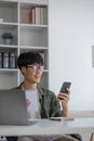 Smart Asian businessman in casual clothing using smartphone and laptop computer working at home office. Male manager Royalty Free Stock Photo