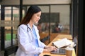 Smart Asian female doctor in a uniform using her laptop, remote working at a cafe Royalty Free Stock Photo