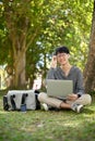 Smart Asian male college student wearing glasses, sits under the tree with his laptop Royalty Free Stock Photo