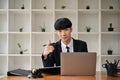 A smart Asian male lawyer in a formal suit points his finger at the camera while sitting at his desk Royalty Free Stock Photo