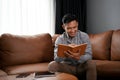 Smart Asian man making list or taking notes on his notebook while sitting on sofa Royalty Free Stock Photo