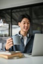 Smart Asian man remote working at the cafe, sipping coffee and working on his project on laptop