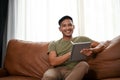 Smart Asian man using his digital tablet while relaxing on a sofa in the living room Royalty Free Stock Photo