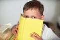 Smart boy with glasses hides his face behind a book with a blue cover Royalty Free Stock Photo