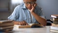 Smart boy in glasses sitting in library reading books, educational literature Royalty Free Stock Photo