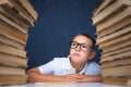 Smart boy in glasses sitting between two piles of books and look away thoughtfully Royalty Free Stock Photo