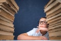 Smart boy in glasses sitting between two piles of books and look away thoughtfully Royalty Free Stock Photo