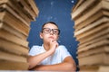 Smart boy in glasses sitting between two piles of books and look down thoughtfully Royalty Free Stock Photo