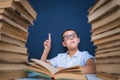 Smart boy in glasses sitting between two piles of books and look up, pointing finger Royalty Free Stock Photo