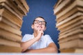 Smart boy in glasses sitting between two piles of books and look up thoughtfully Royalty Free Stock Photo