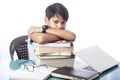 Smart boy looking at camera laying on pile of books and laptop on desk Royalty Free Stock Photo