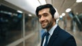 Smart business man wearing headphone while standing at train station. Exultant. Royalty Free Stock Photo