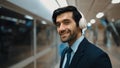 Smart business man wearing headphone while standing at train station. Exultant. Royalty Free Stock Photo