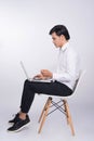 Smart casual asian man seated on chair, using laptop in studio b Royalty Free Stock Photo