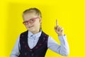 Smart Caucasian girl with glasses stands on a yellow background with a place for the text.