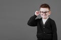 Smart child boy adjusts his glasses with finger on the grey background, close-up. Studio juvenile portrait in casual clothes. copy Royalty Free Stock Photo