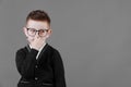 Smart child boy adjusts his glasses with finger on the grey background, close-up. Studio juvenile portrait in casual Royalty Free Stock Photo