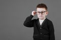 Smart child boy adjusts his glasses with finger on the grey background, close-up. Studio juvenile portrait in casual Royalty Free Stock Photo