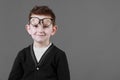 Smart child boy adjusts his glasses and having fun on the grey background, close-up. Studio juvenile portrait in casual clothes. Royalty Free Stock Photo