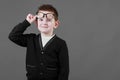 Smart child boy adjusts his glasses and having fun on the grey background, close-up. Studio juvenile portrait in casual Royalty Free Stock Photo