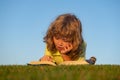 Smart child reading book, laying on grass in field on sky background. Portrait of clever kids outdoor. Royalty Free Stock Photo