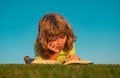 Smart child reading book, laying on grass in field on sky background. Portrait of clever kids outdoor. Royalty Free Stock Photo