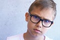 Smart concerned boy with eye blue light blocking glasses looking to camera. Grunge gray wall background Royalty Free Stock Photo