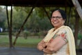 Smart and confident senior north Indian woman standing, posing for the camera with hands crossed / folded in a park wearing an off