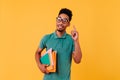 Smart curly guy with books posing with smile. Indoor shot of interested african student isolated on