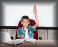 A smart, cute boy raises his hand to answer in class. Happy child against a white board. Education concept