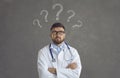 Doctor with question marks above head standing arms crossed and thinking about patient's diagnosis Royalty Free Stock Photo