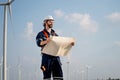 Smart engineer or technician man stand with holding drawiing paper and look forward in front of windmill or wind turbine cluster Royalty Free Stock Photo