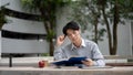 A smart and focused Asian male university student is reading a book in a campus park Royalty Free Stock Photo