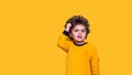 Smart funny curly kid scratches his head while thinking. Little wunderkind ready to go to school isolated on yellow