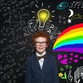 Smart funny little boy wearing glasses and blue suit on background with question marks, lightbulb, question marks Royalty Free Stock Photo
